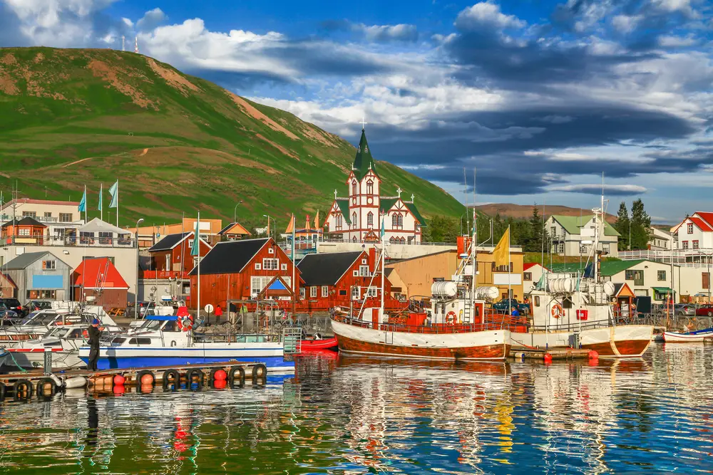 Coastal view of the Husavik village in Iceland with colonial homes and boats in the harbor as we detail how long are flights to Iceland