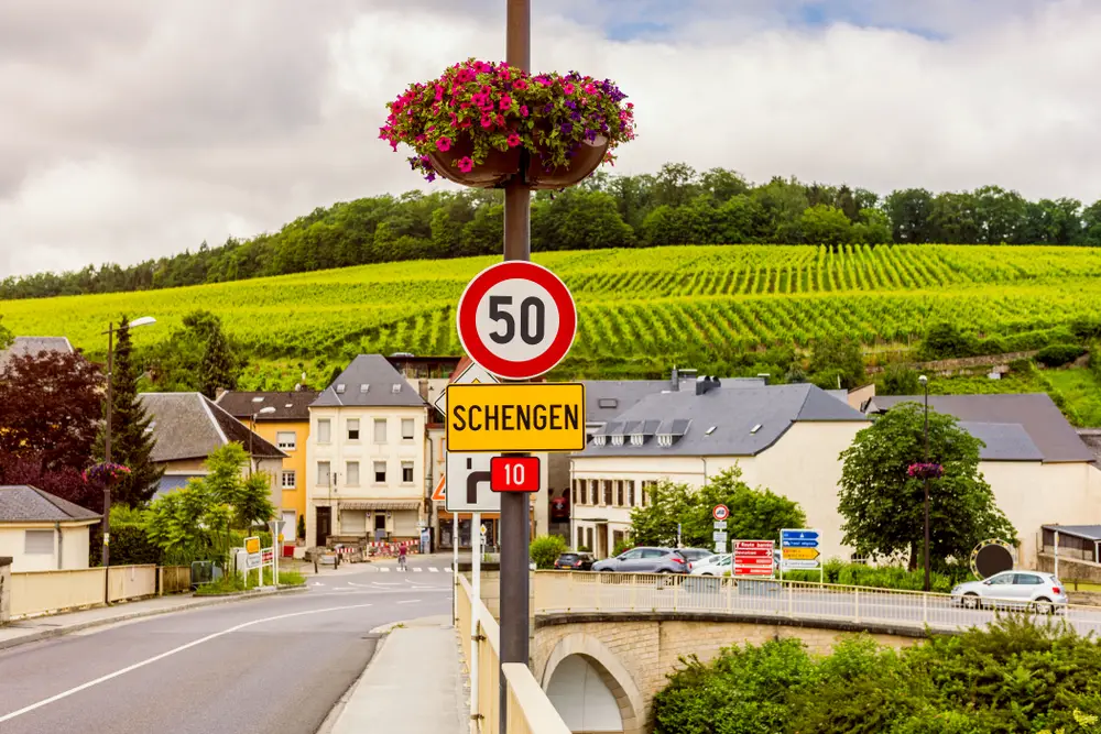 A road sign that says Schengen and in background is a wide vineyard. 