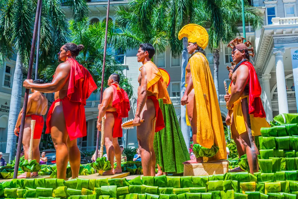 Αναπαράσταση ιστορικών γεγονότων και ηγεμόνων της Χαβάης με ανθρώπους ντυμένους με παραδοσιακά ρούχα και τελετουργικά ρούχα κατά τη διάρκεια της Ημέρας Παρέλασης του Βασιλιά Kamehameha για ένα κομμάτι που συζητούσε πότε η Χαβάη έγινε πολιτεία