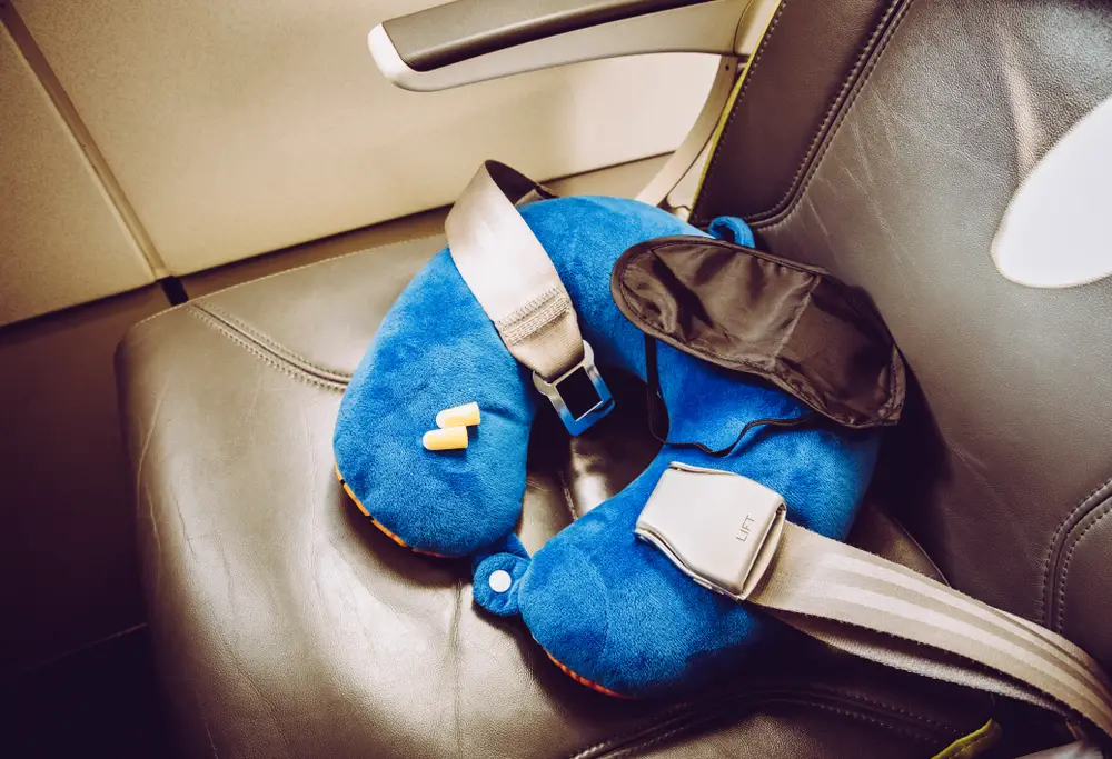 Έννοια του τι είναι μια πτήση με κόκκινα μάτια που απεικονίζεται με ένα κάθισμα αεροπλάνου που περιέχει ένα μαξιλάρι λαιμού, μάσκα ύπνου και ωτοασπίδες για μια ολονύκτια πτήση