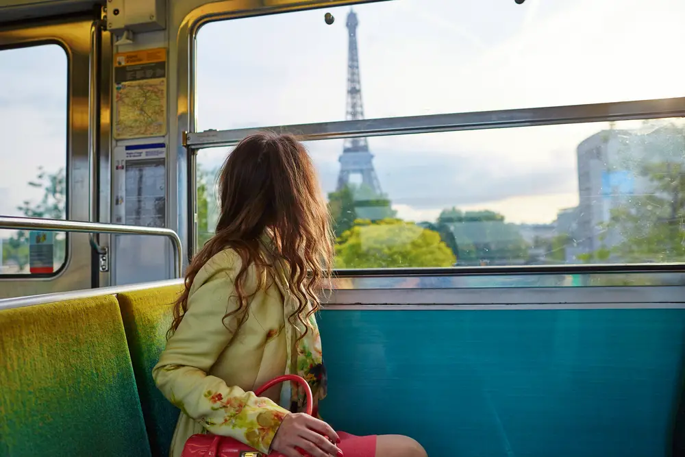 Woman looking out the window of a Paris train at the Eiffel Tower, showing one reason you should travel Europe by train
