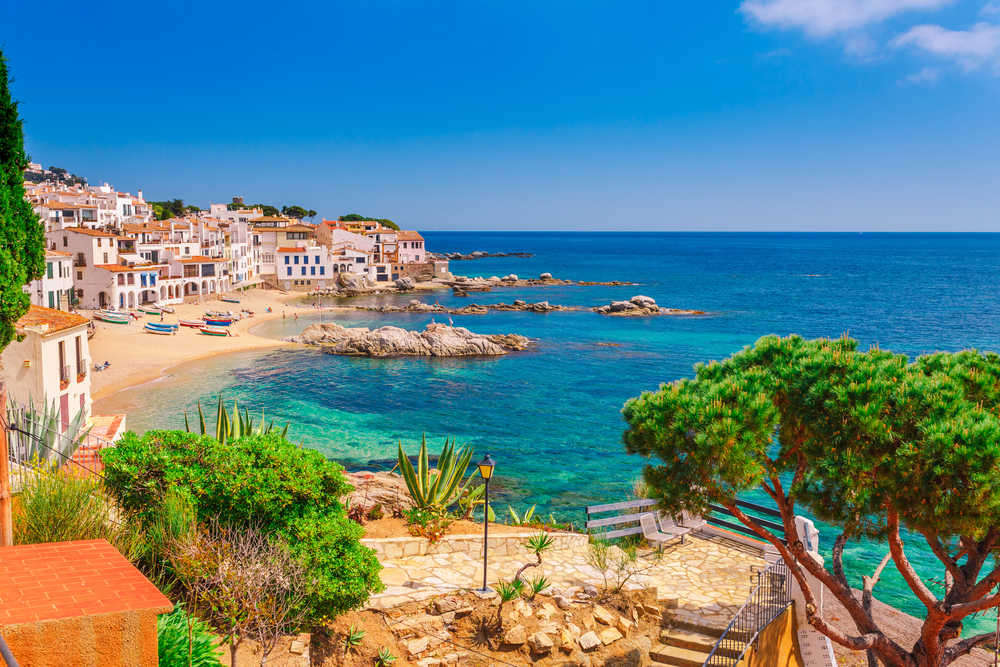 Beautiful shot of a beach in Catalonia, Spain near Barcelona with hotels and trees around the golden sand beach for a Spain vs Portugal comparison guide