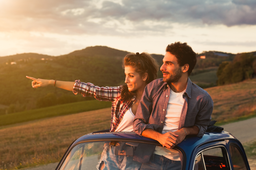 Ένα ζευγάρι που παρακολουθεί το ηλιοβασίλεμα, όπου η γυναίκα δείχνει προς μια συγκεκριμένη κατεύθυνση, ενώ το πάνω μισό του σώματός τους είναι έξω είναι η ηλιοροφή του αυτοκινήτου. 