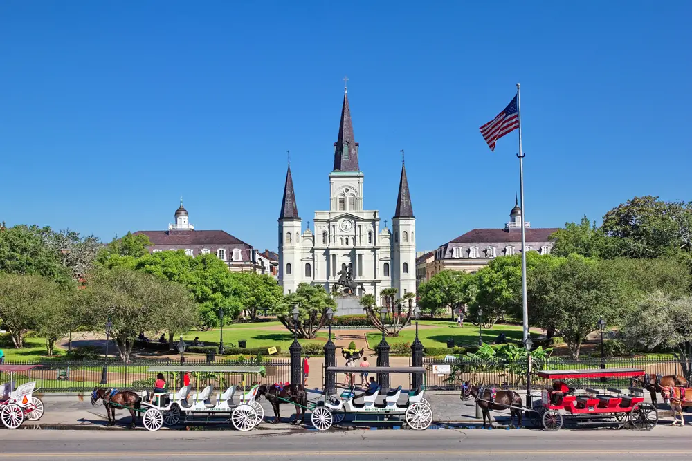 Προσεγμένο παλιό αρχοντικό στην πλατεία Τζάκσον με άμαξες αλόγων έξω από τη μαύρη περιφραγμένη αυλή για οδηγό με τίτλο Is New Orleans Safe to Visit