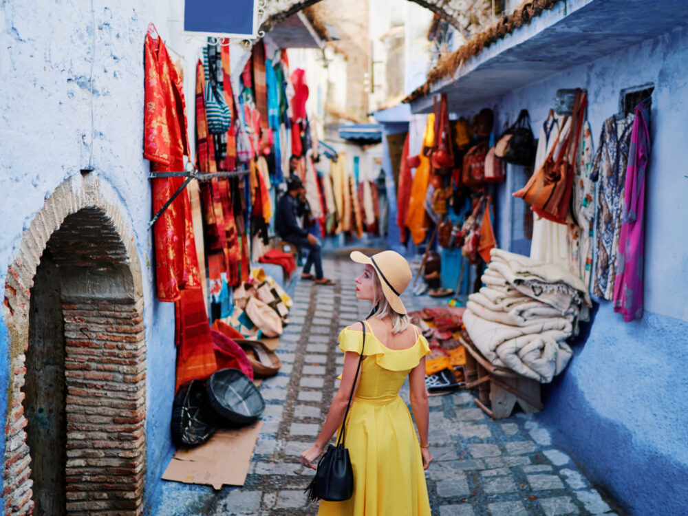 Πολύχρωμα ρούχα σε μια αγορά όπως τα βλέπει μια γυναίκα με κίτρινο φόρεμα για ένα κομμάτι με τίτλο Is Morocco Safe