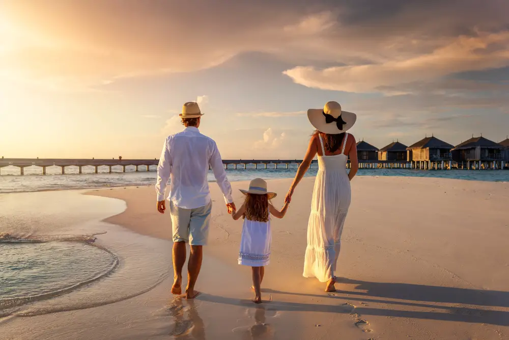 Μια οικογένεια, φορώντας ρούχα παραλίας, περπατώντας στην παραλία κατά τη διάρκεια του ηλιοβασιλέματος. 