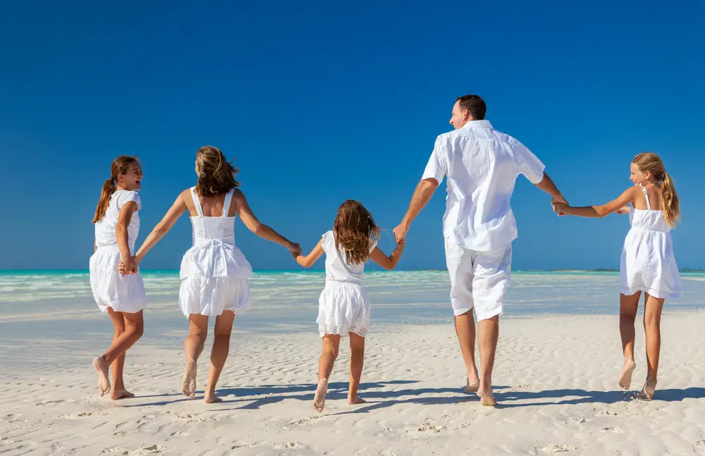 Μια πενταμελής οικογένεια, όλοι φορώντας λευκά στην παραλία, κρατώντας ο ένας το χέρι του άλλου τρέχοντας στην ακτή. 