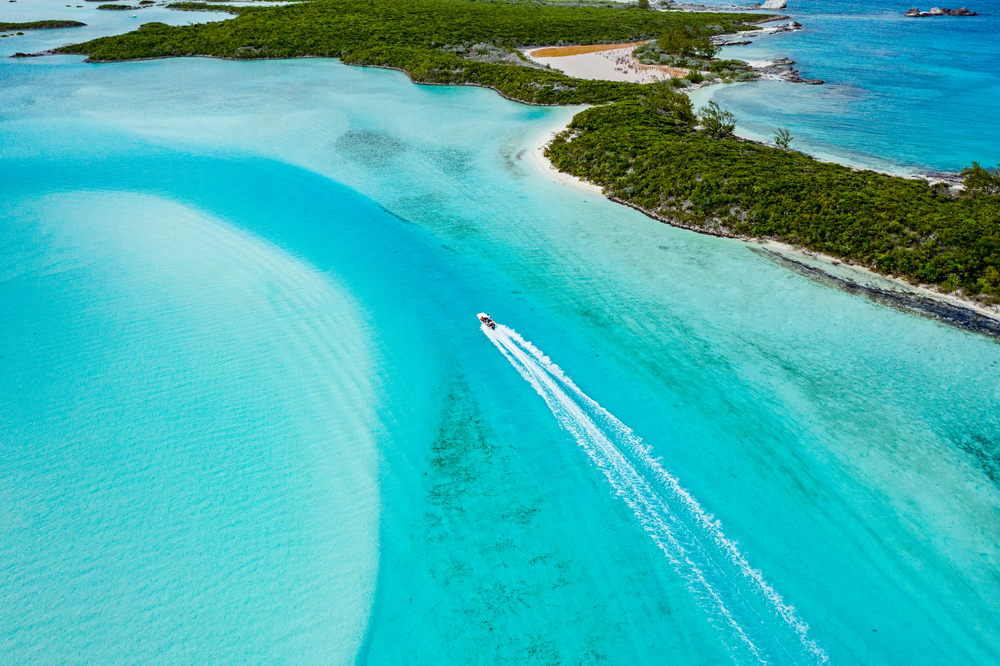 Αεροφωτογραφία ενός νησιού με κρυστάλλινα νερά και λευκή άμμο, όπου στα νερά του φαίνεται ταχύπλοο. 