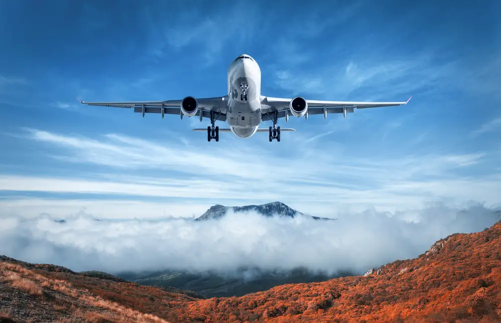 Καλλιτεχνική φωτογραφία ενός αεροπλάνου που πετά πάνω από τη χρωματιστή κοιλάδα του φθινοπώρου με τα σύννεφα στον ουρανό για έναν οδηγό που συγκρίνει την Booking.com και την Expedia