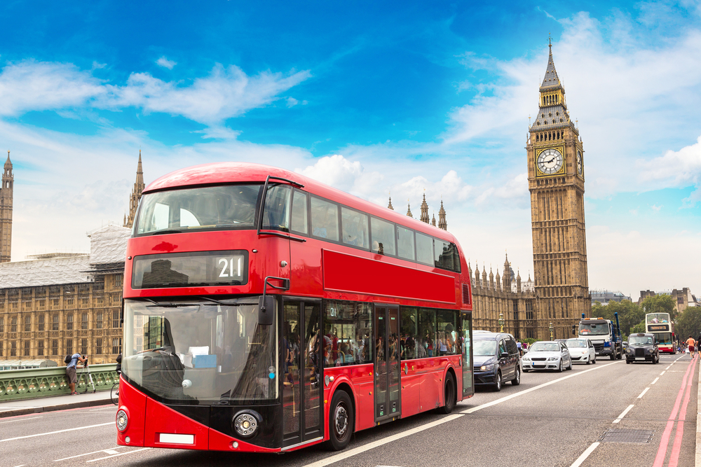 Διώροφο κόκκινο λεωφορείο ταξιδεύει στο Λονδίνο με το Μπιγκ Μπεν στο φόντο για μια ενότητα που δείχνει πώς να κάνετε κράτηση για αξιοθέατα στην Expedia και την Booking.com