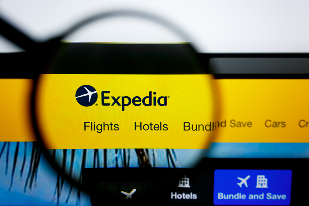 Οθόνη φορητού υπολογιστή με μεγεθυντικό φακό πάνω από το λογότυπο της Expedia που δείχνει πτήσεις και ξενοδοχεία για έναν οδηγό σύγκρισης Booking.com εναντίον Expedia