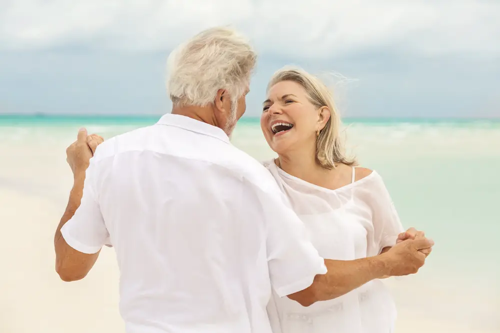 Δύο ηλικιωμένο ζευγάρι φορώντας λευκά ρούχα, που χορεύουν στην παραλία.