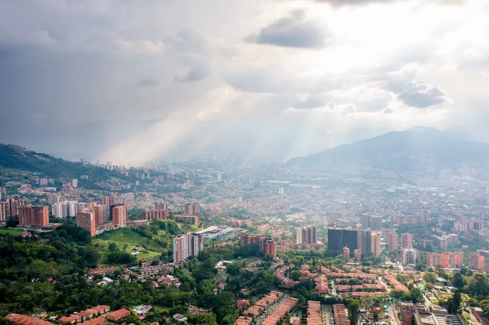 Rain above the city of Medellin during the wet season, the overall worst time to visit, with rays of sun beaming down from the clouds