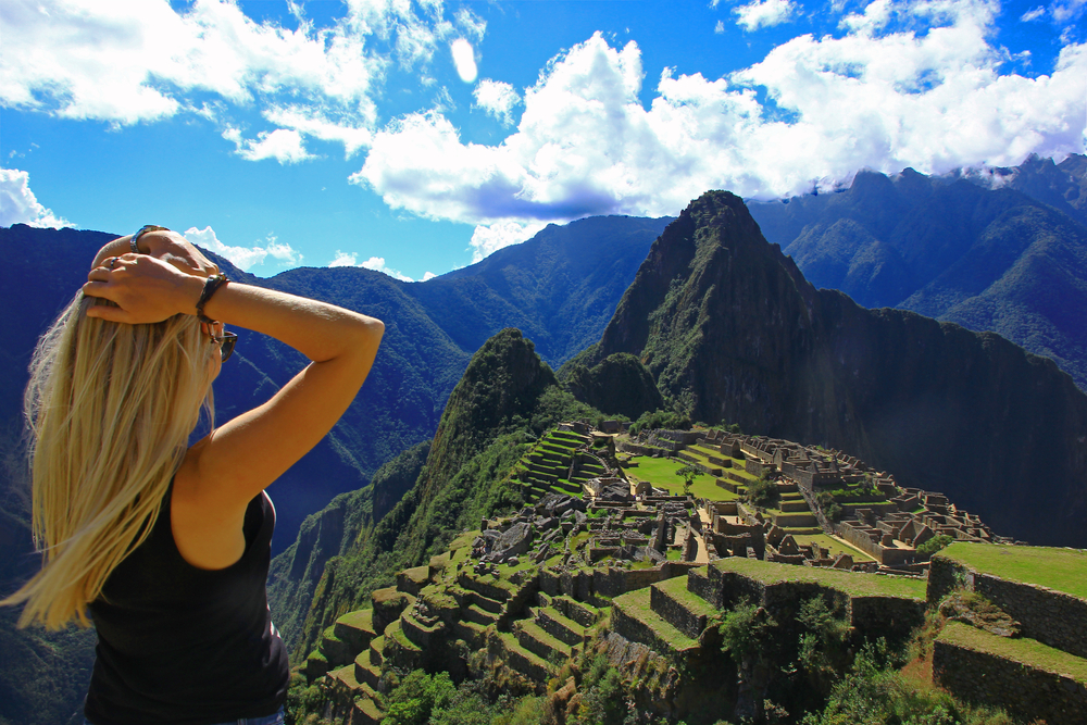 Γυναίκα με μπλε πουκάμισο που κρατά το κεφάλι της την καλύτερη στιγμή για να επισκεφθείτε το Μάτσου Πίτσου, με έναν μπλε ουρανό πάνω από το βουνό