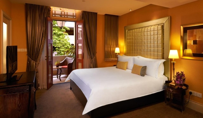Ένα τολμηρά διακοσμημένο δωμάτιο ξενοδοχείου με πορτοκαλί τοίχους και ένα μεγάλο χρυσό κεφαλάρι στο ξενοδοχείο The Scarlet στη Σιγκαπούρη