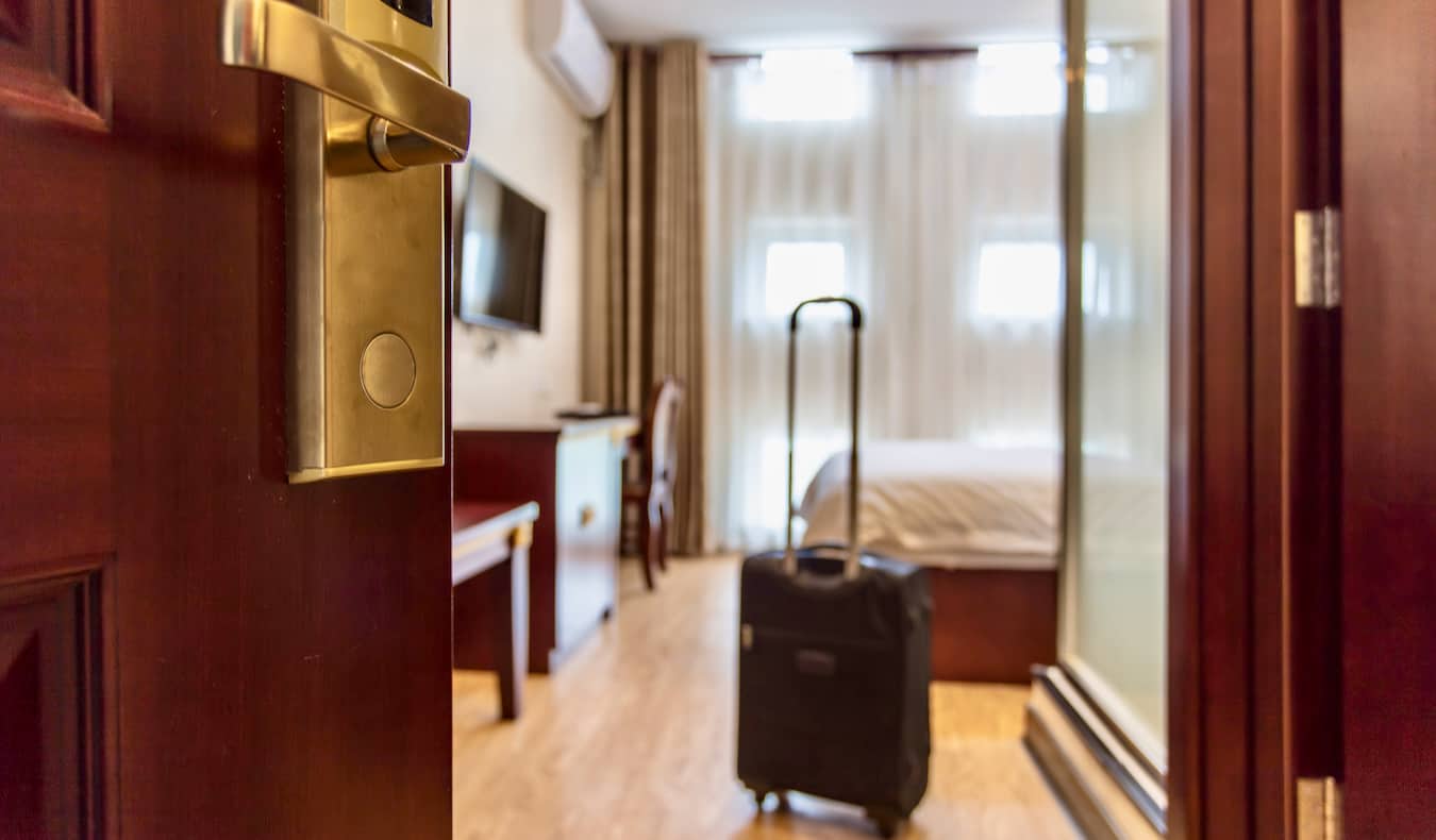 Μια μικρή κυλιόμενη βαλίτσα που στέκεται κοντά στην πόρτα σε ένα άνετο δωμάτιο ξενοδοχείου στο εξωτερικό