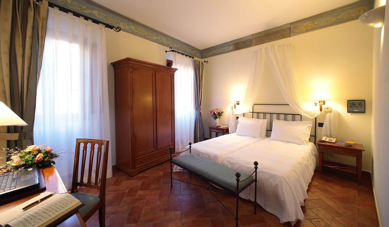 ένα δωμάτιο ξενοδοχείου με δύο μονά κρεβάτια το ένα δίπλα στο άλλο, ένα γραφείο, μια ξύλινη ντουλάπα, δάπεδα με πλακάκια από τερακότα και απαλό φωτισμό, στο Hotel Davanzati στη Φλωρεντία, Ιταλία
