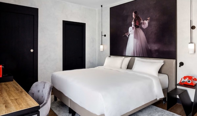 Ένας μεγάλος πίνακας κρέμεται πάνω από ένα διπλό κρεβάτι σε ένα δωμάτιο ξενοδοχείου με ξύλινο γραφείο και κόκκινο περιστροφικό τηλέφωνο στο κομοδίνο στο Radisson RED Madrid στη Μαδρίτη, Ισπανία